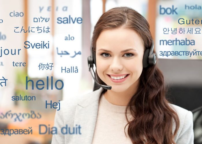 translation, business and technology concept - smiling female translator or operator in headset at office over greeting words in different foreign languages